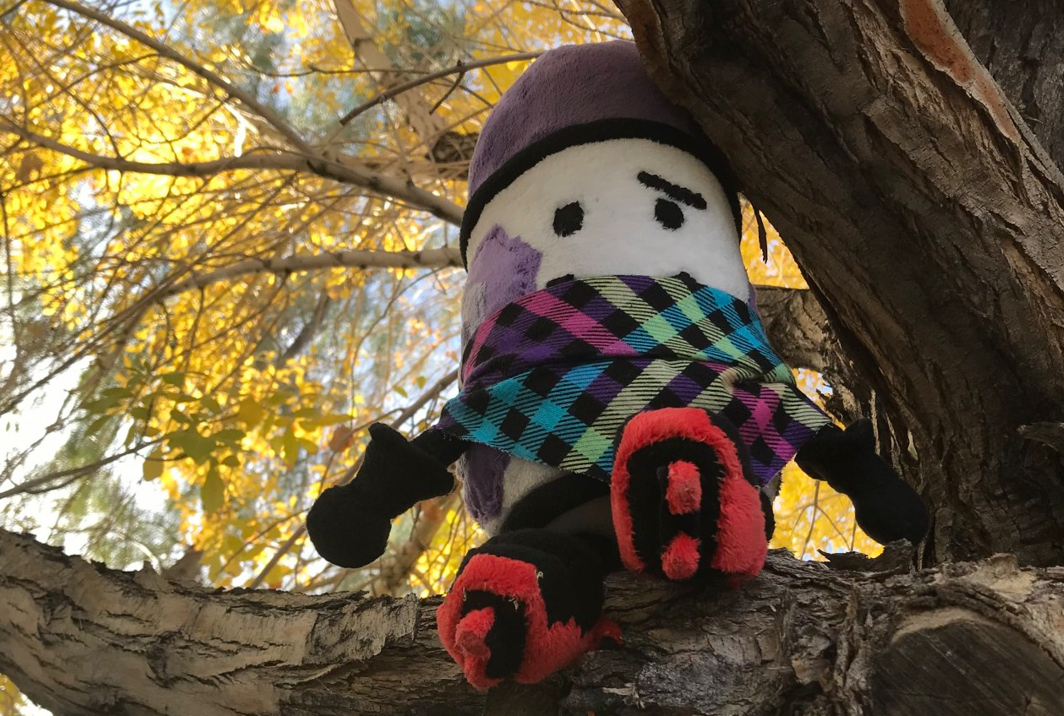 A handmade plush sitting on the branch of a tree.