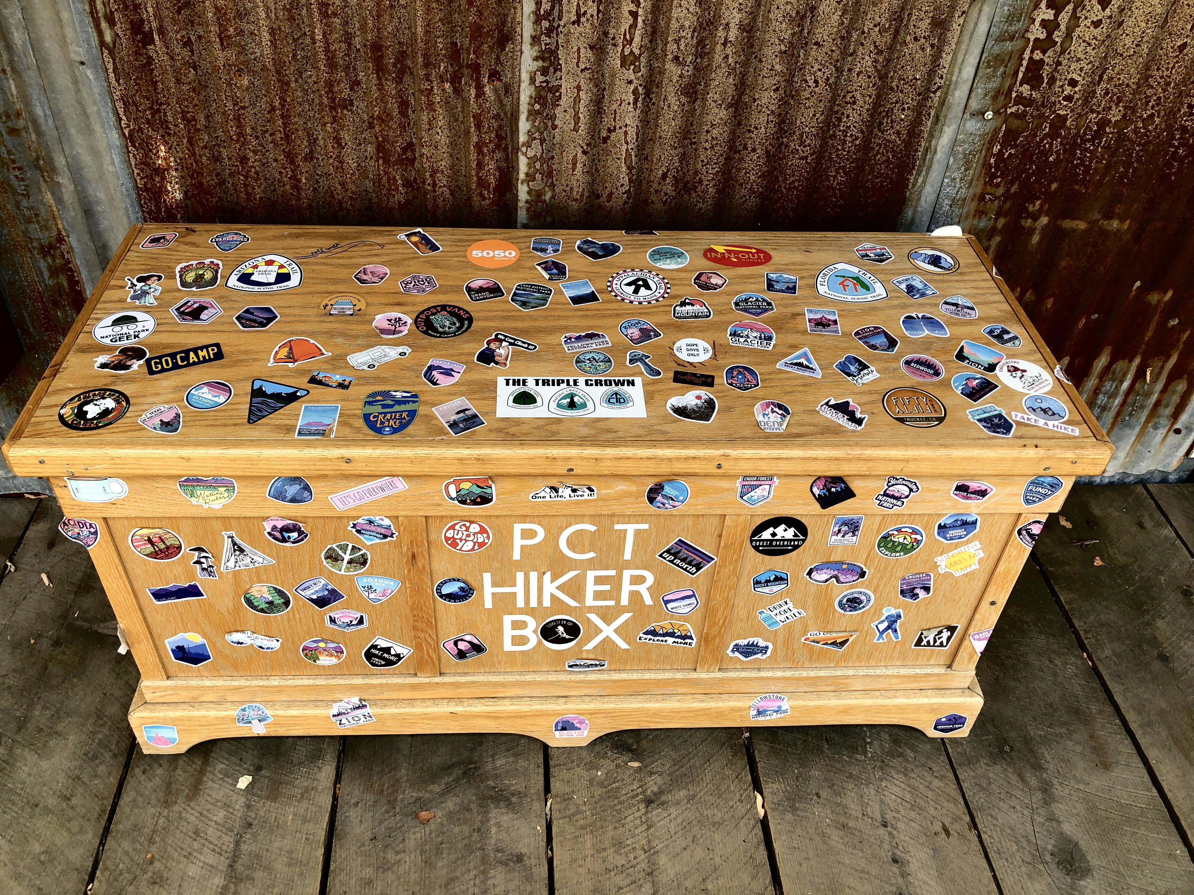 a wooden box covered in stickers and a label reading PCT hiker box