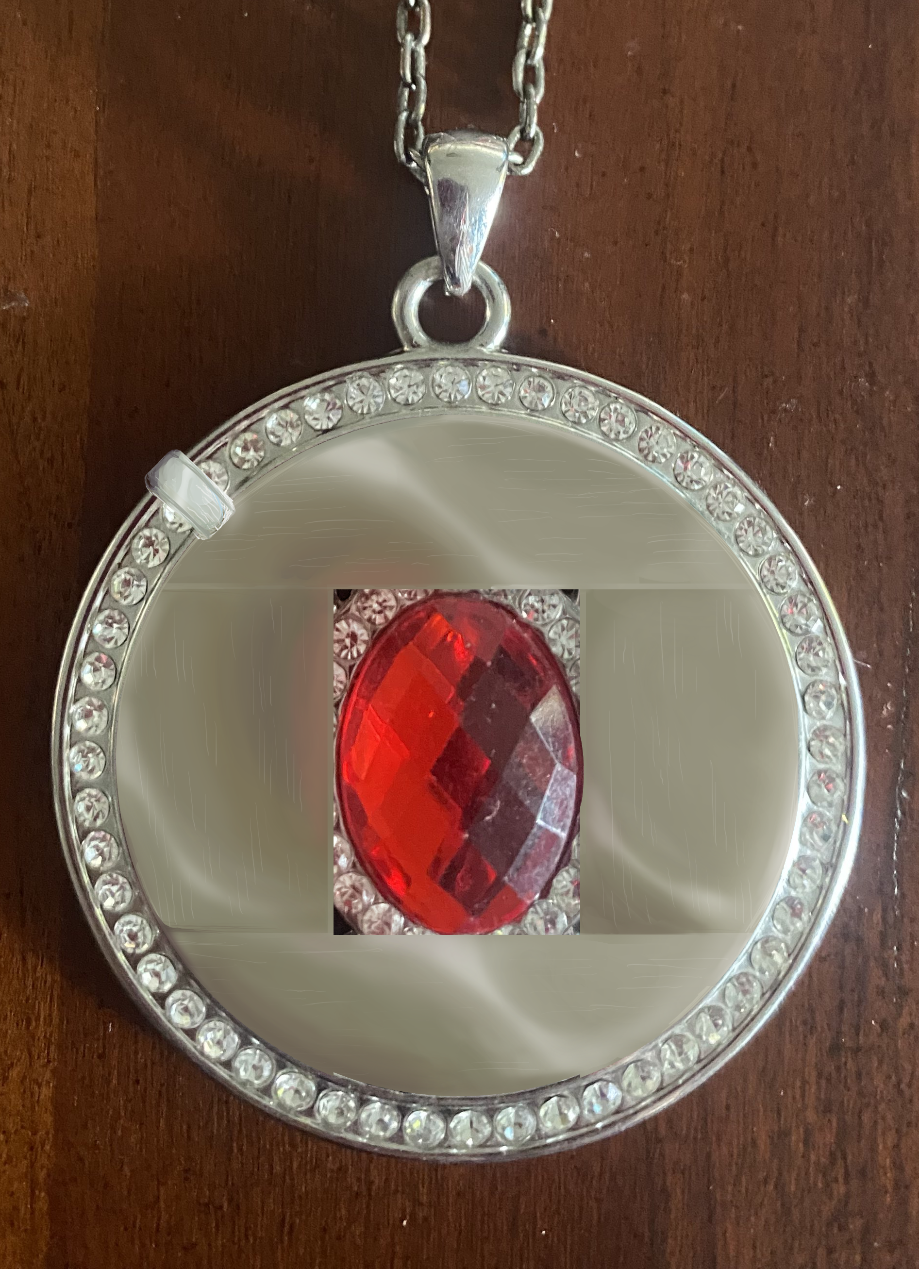 An amulet with metal plates on its surface, a central red gem, and a ring connected to its circumference.
