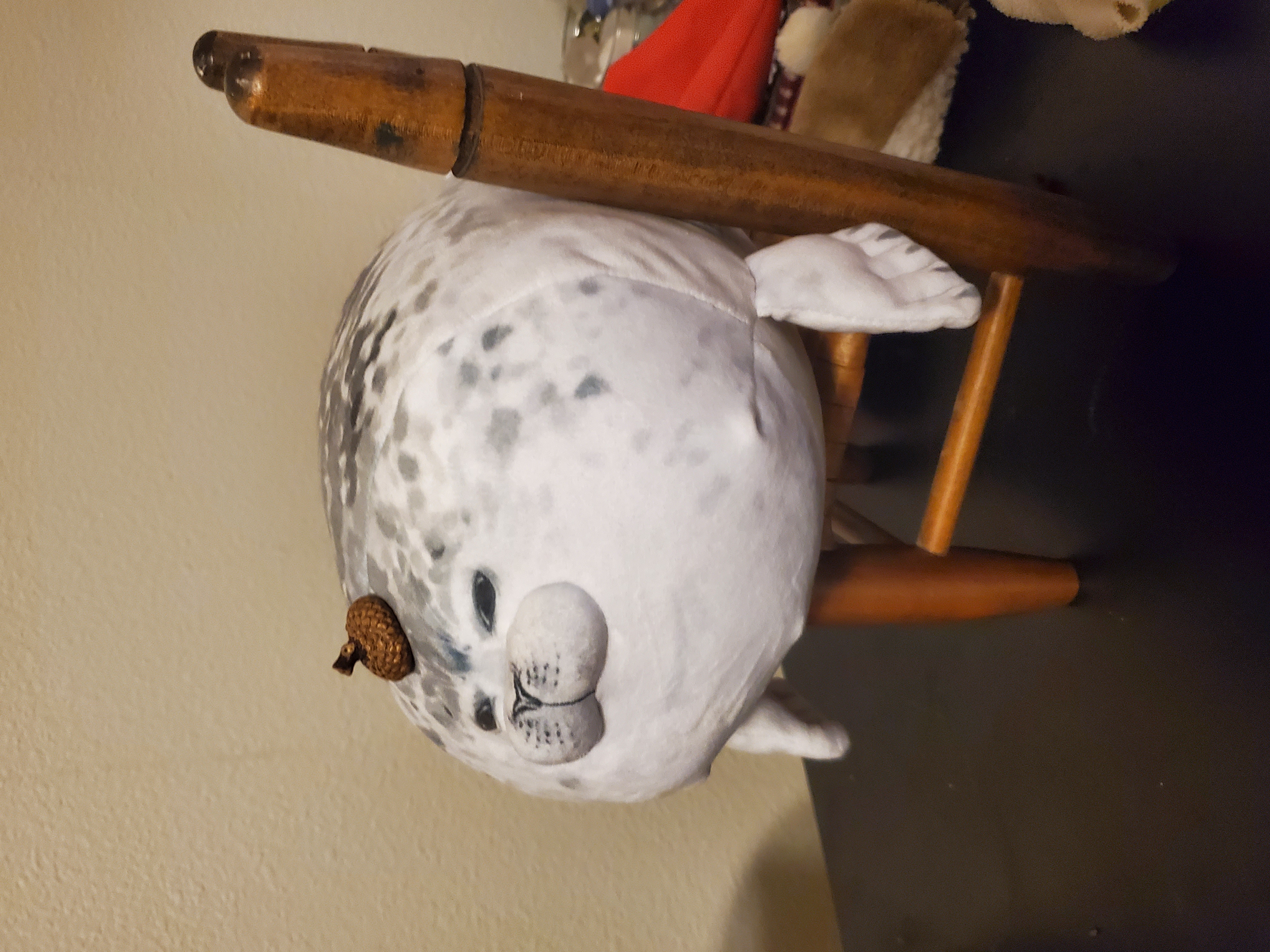 image of a rotund seal plushie. it is speckled dark gray, with little blueish white flippers stitched to its body. it has squinty little eyes and an acorn-top placed on it's head. it is also sitting on a minature chair