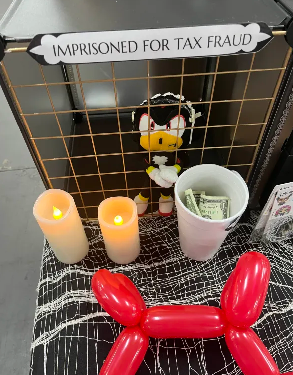 Shadow the Hedgehog plushie locked in a mini makeshift prison, imprisoned for tax fraud. Next to him is a tip 