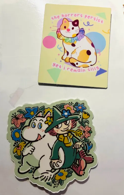 Two stickers illustrated by mussyhead and an unknown artist. Mussyhead's sticker depicts a clown kitty, with the caption 