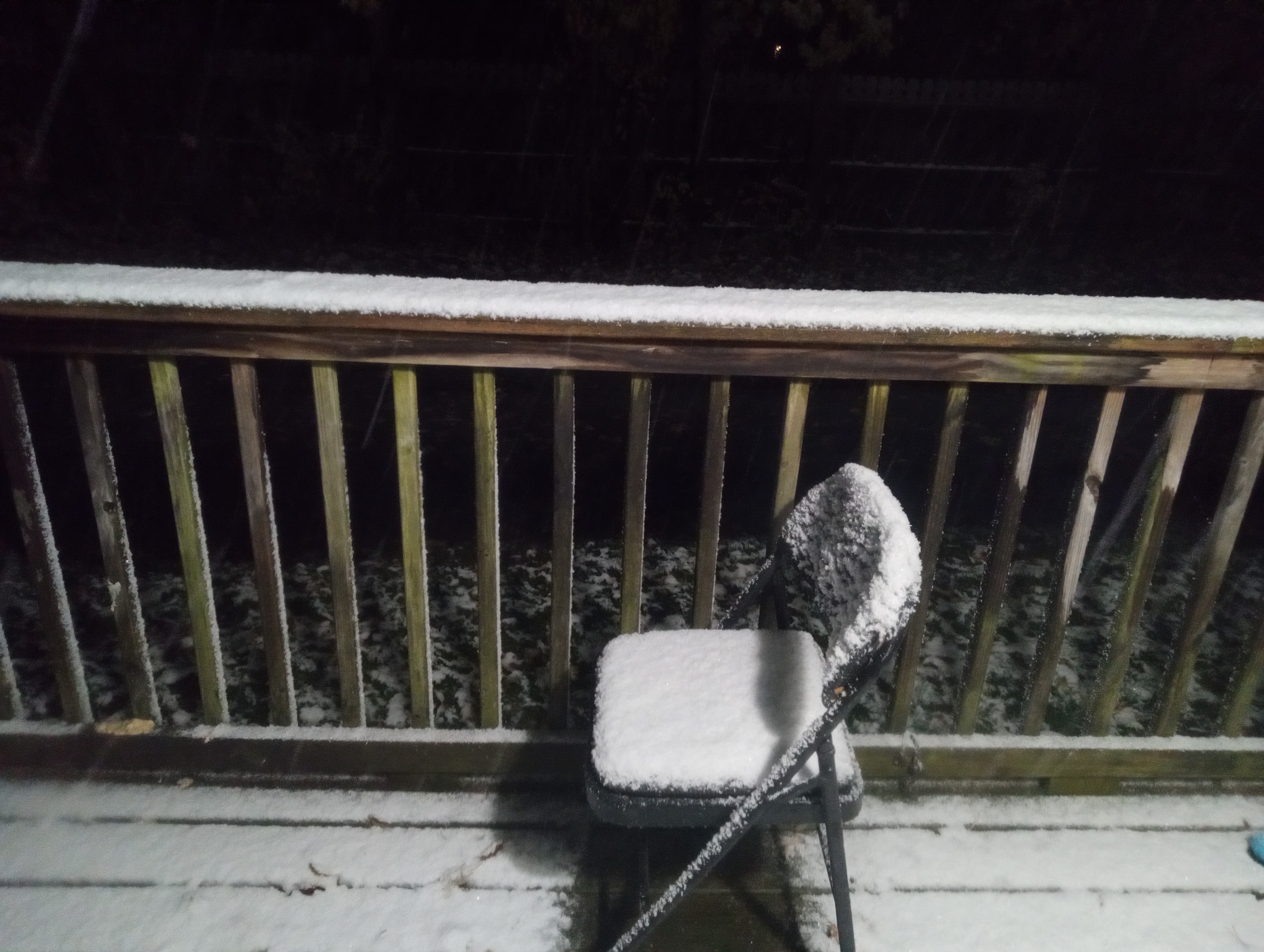 an image taken at night from the front door showing my porch covered in snow. snow is still falling