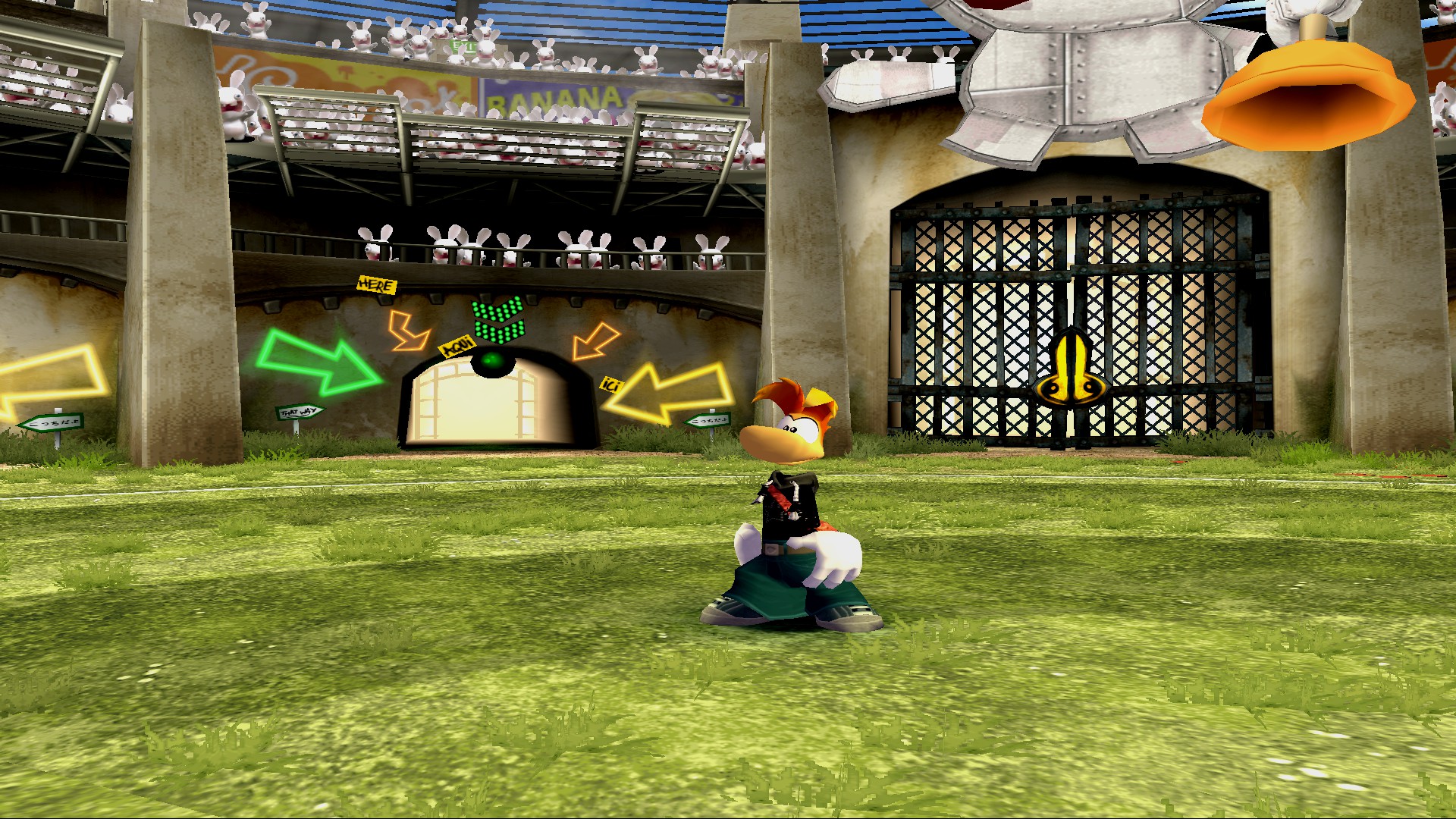 Rayman stands in a grimy arena on a bright sunny day.