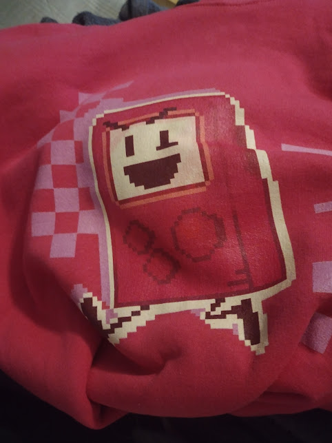 A pink Pixel Brain hoodie, wrapped up on a flat surface.