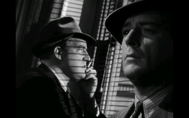 A screencap from I Wake Up Screaming, showing 2 men in fedoras in a dark-lit room. One of them is looking out the window while the other stares into space.