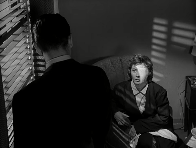 A screencap from The Big Heat, depicting a young lady with half her face covered in bandages looking at a man standing in front of her.