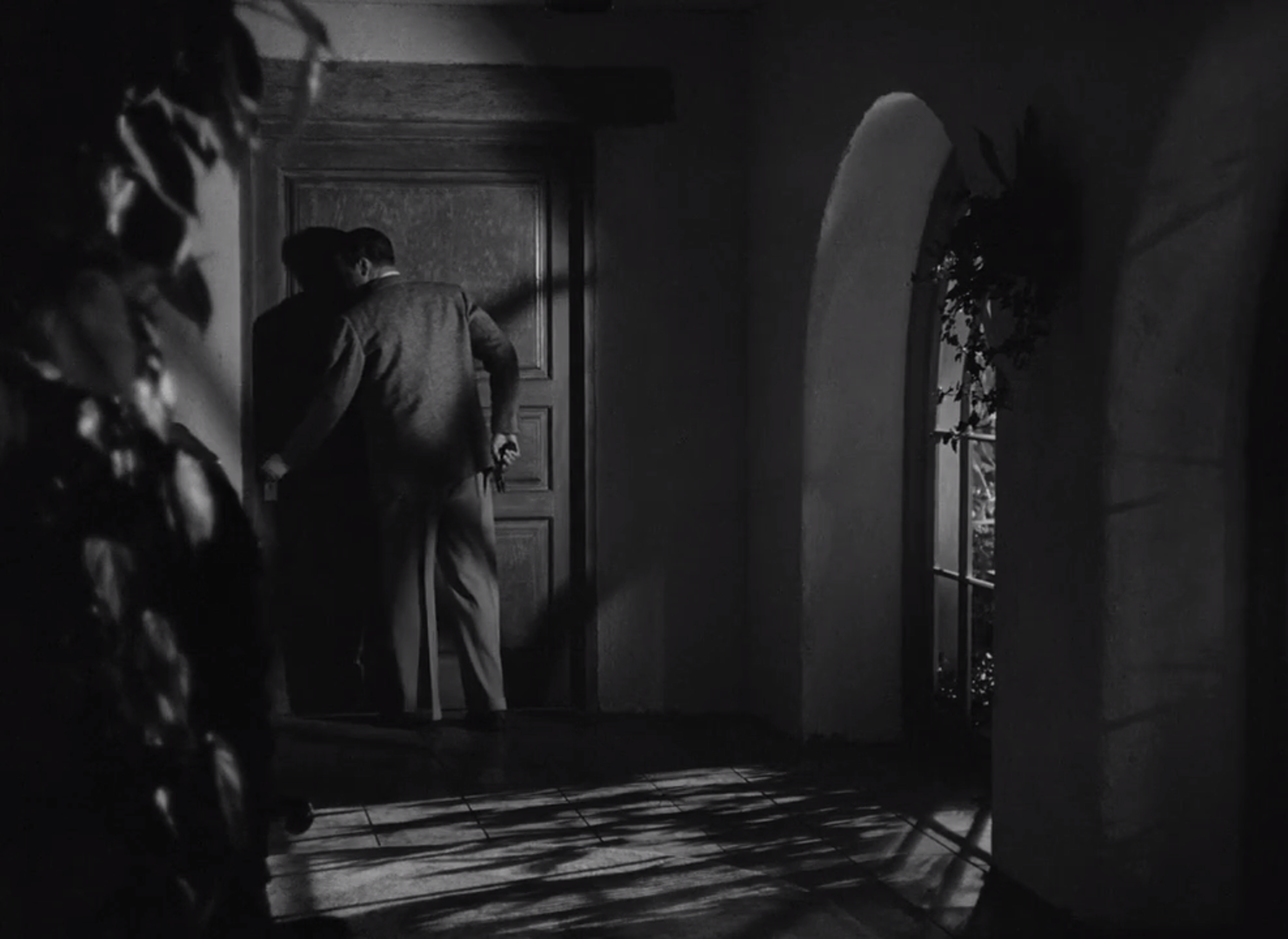 A screencap from They Won't Believe Me. Lawrence 'Larry' Ballantine, forever a loner, slowly opens a door inside his ranch on a cool night.