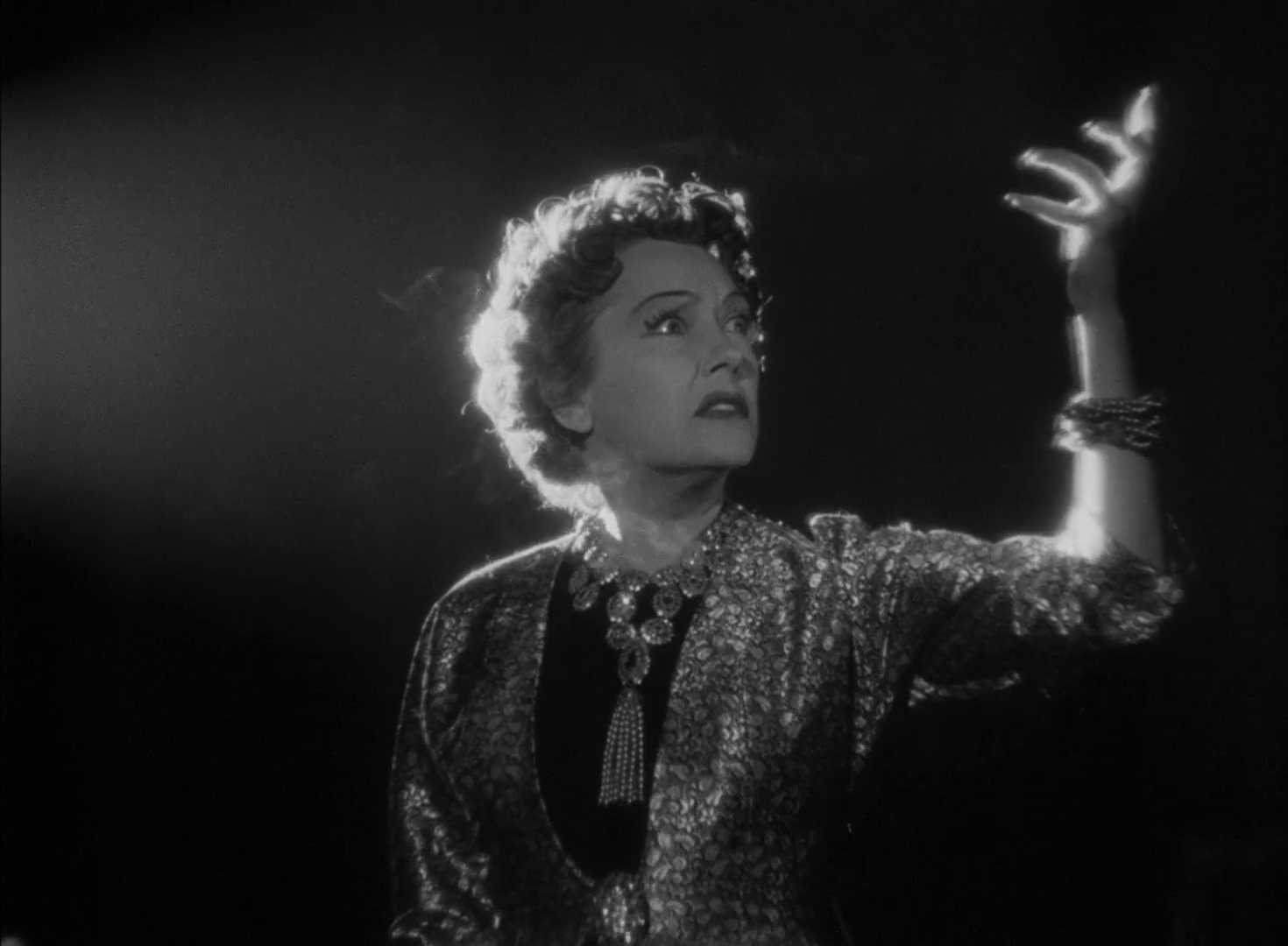 A screencap from Sunset Boulevard. Norma Desmond (Gloria Swanson) strikes a dramatic pose in the dark, backlit only by the strong light of a film projector off-screen.