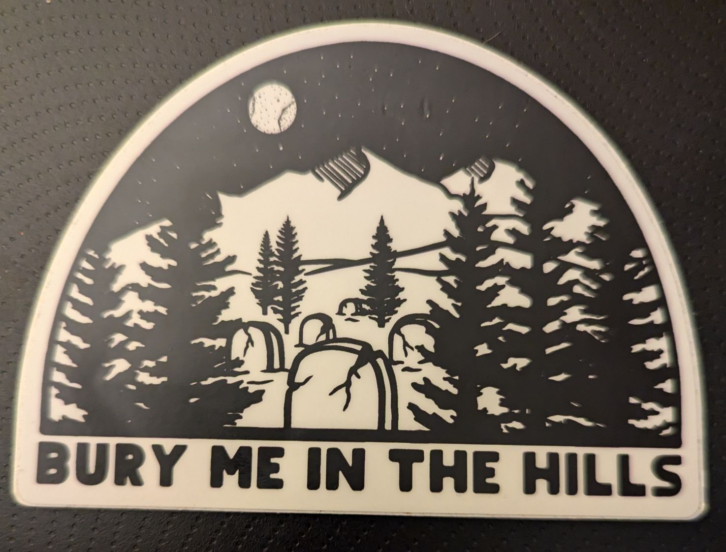 A sticker showing a graveyard in the mountains saying 'bury me in the hills'