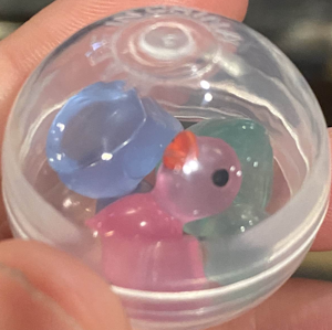 clear plastic ball with three small translucent ducks in it. there is a blue, green, and pink duck.