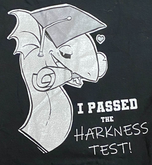 black t-shirt with a white and gray eel monster wearing a graduation cap holding a diploma at its mouth looking seductively at the camera with text that says i passed the harkness test