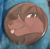 Pin-back button of a brown wolf man with one  silver eye and one brown eye sticking his tongue out smiling at the camera