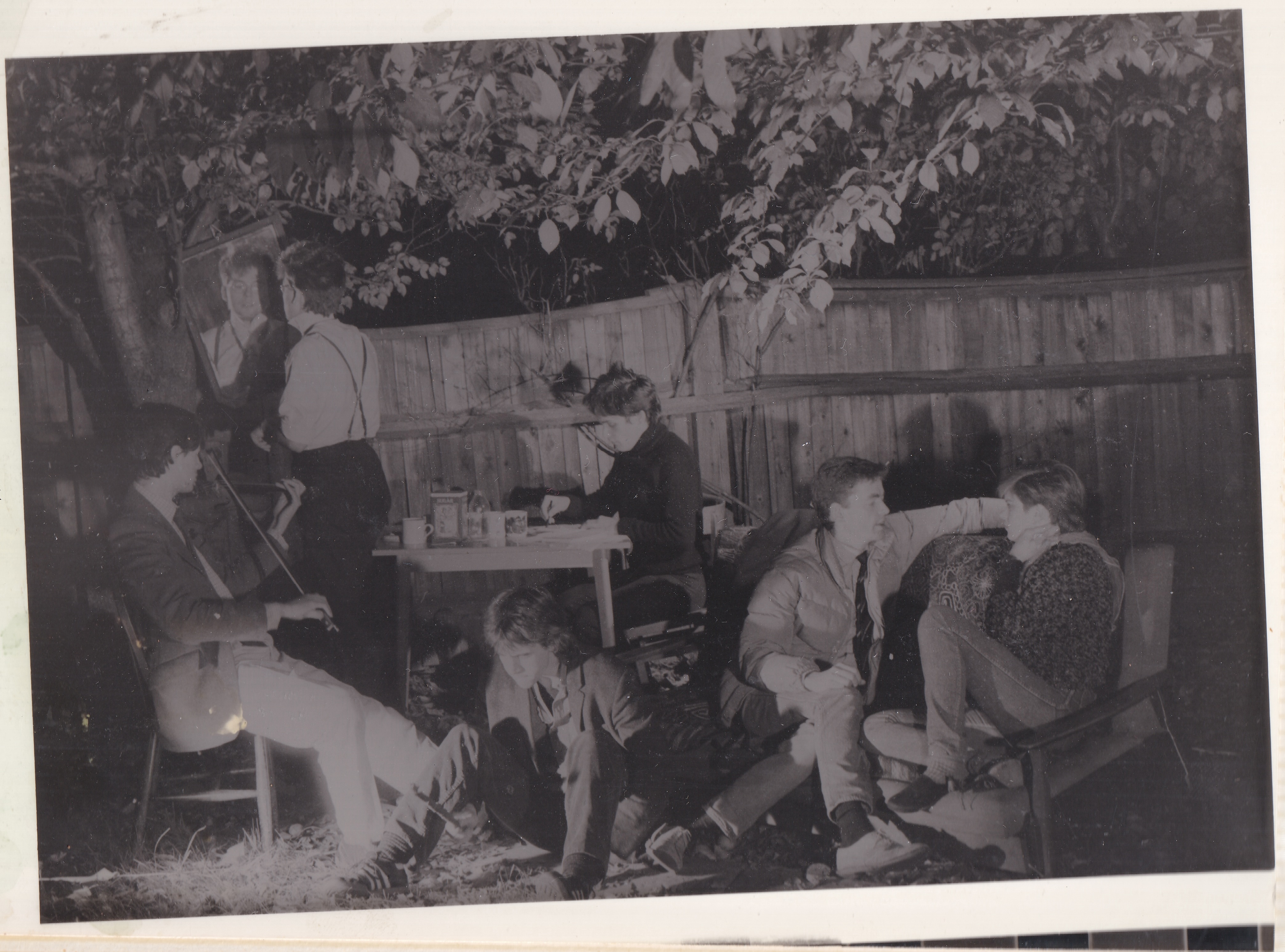 The band sitting outside in their backyard on various chairs.