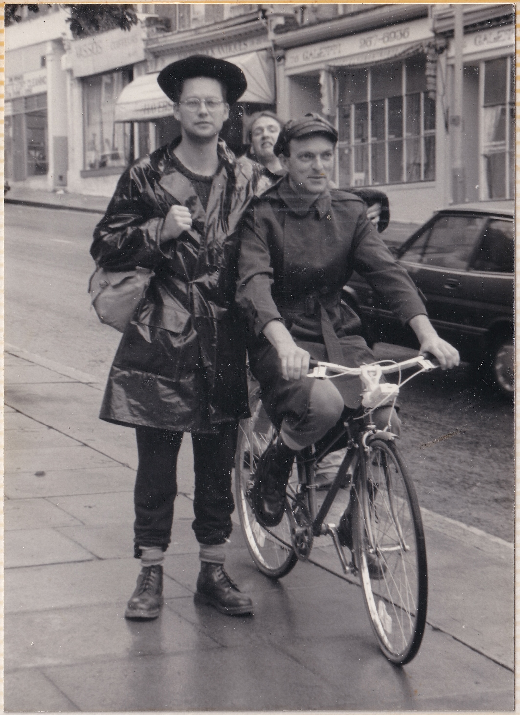 Jon stands next to Kim who is on a bike. In between them someone photobombs.