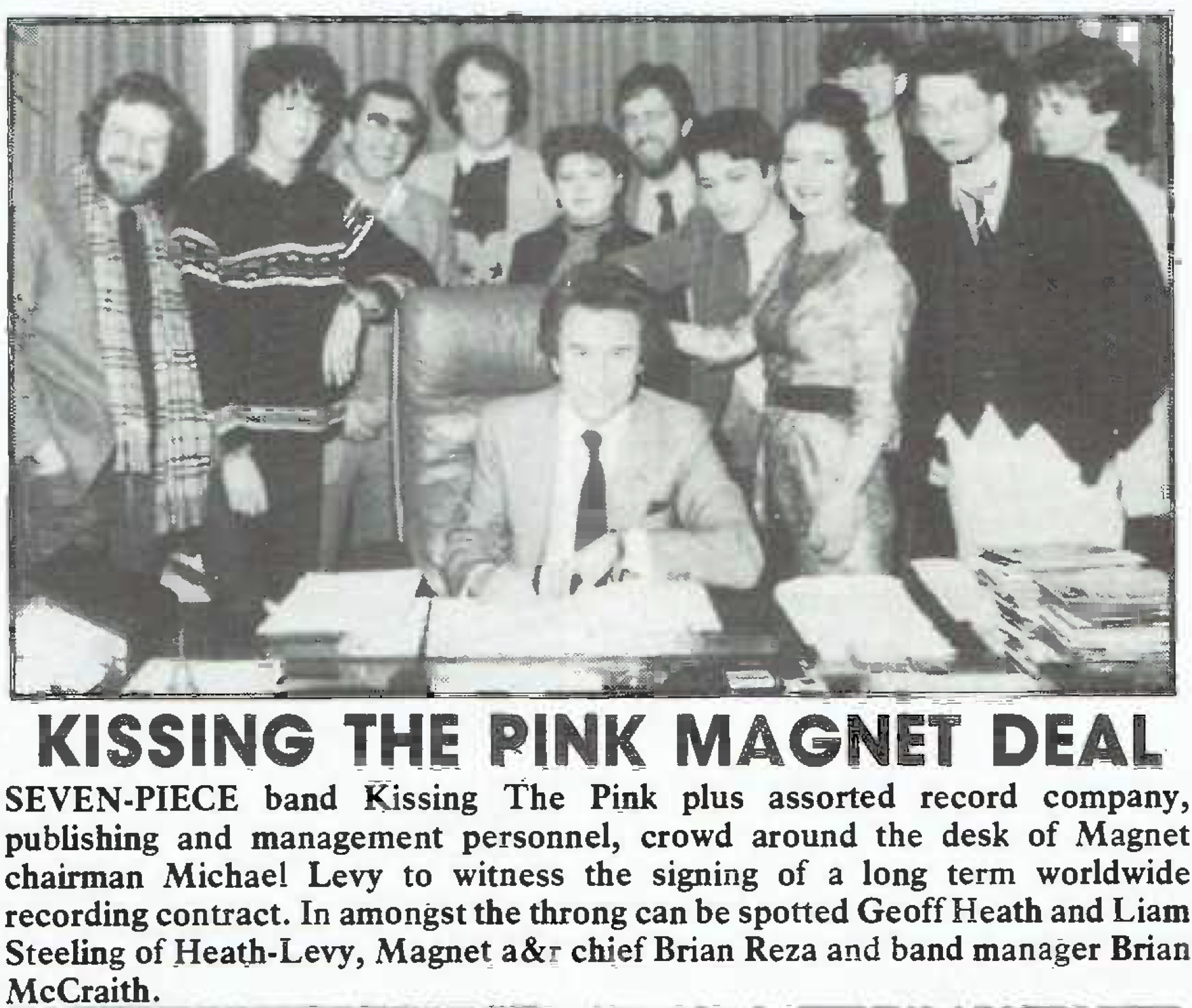 A low-quality black and white scan of a magazine clipping, which has a photo of Kissing the Pink's 7-member Naked lineup along with some higher ups from Magnet Records. Seated is Magnet A&R head Brian Reza. Behind him, Left to right stands: Eddie Levy (Magnet), Peter Barnett, Liam Teeling (Magnet), Michael McCraith (Magnet), Jo Wells, Geoff Heath (Magnet), George Stewart, Sylvia Griffin, Nick Whitecross, Jon Hall and Stevie Cusack. Below the image is text, which is transcribed below.