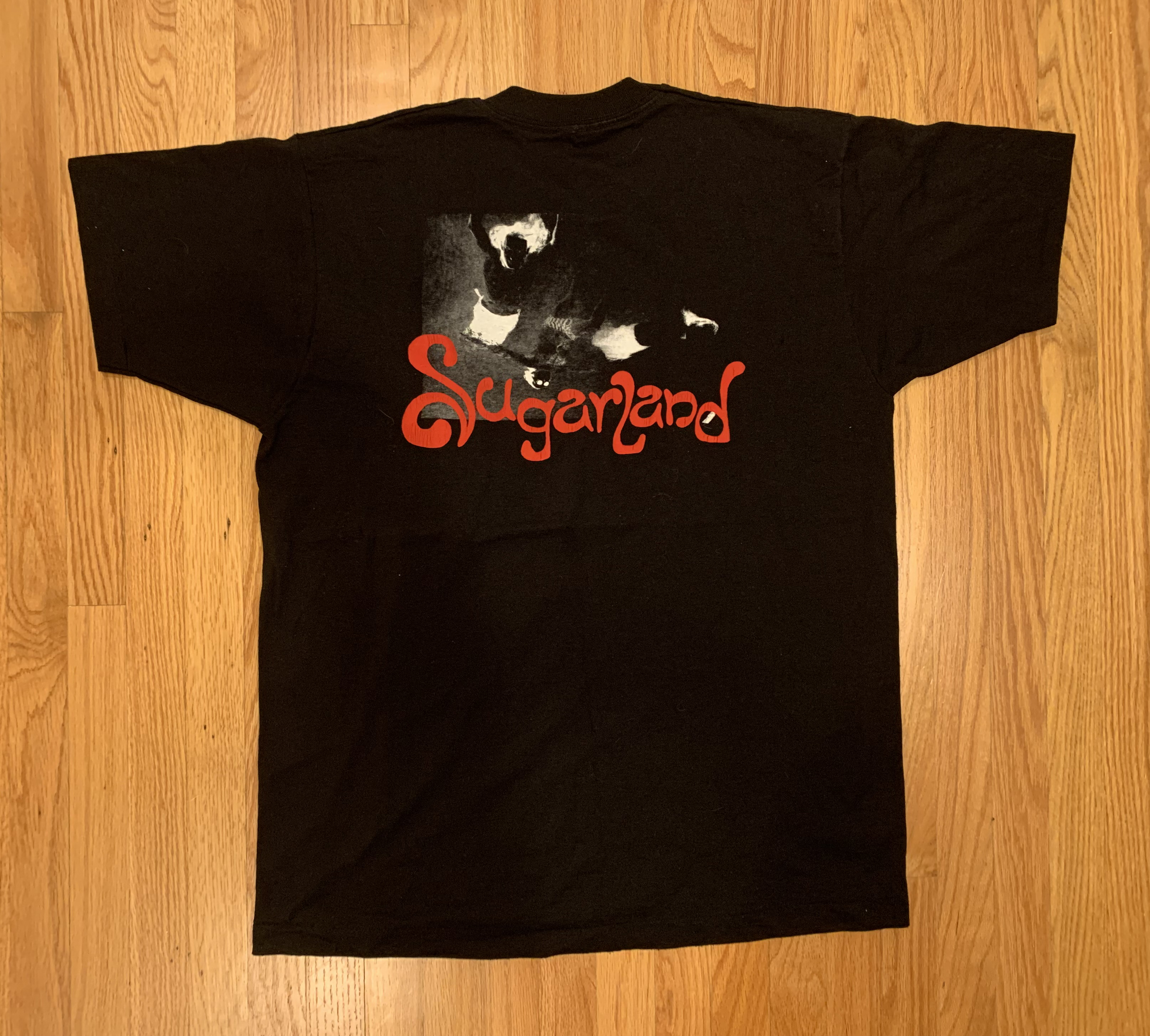 A black shirt with a unique red sugarland logo in front of a blackened contrasted version of the initial sugarland album cover
