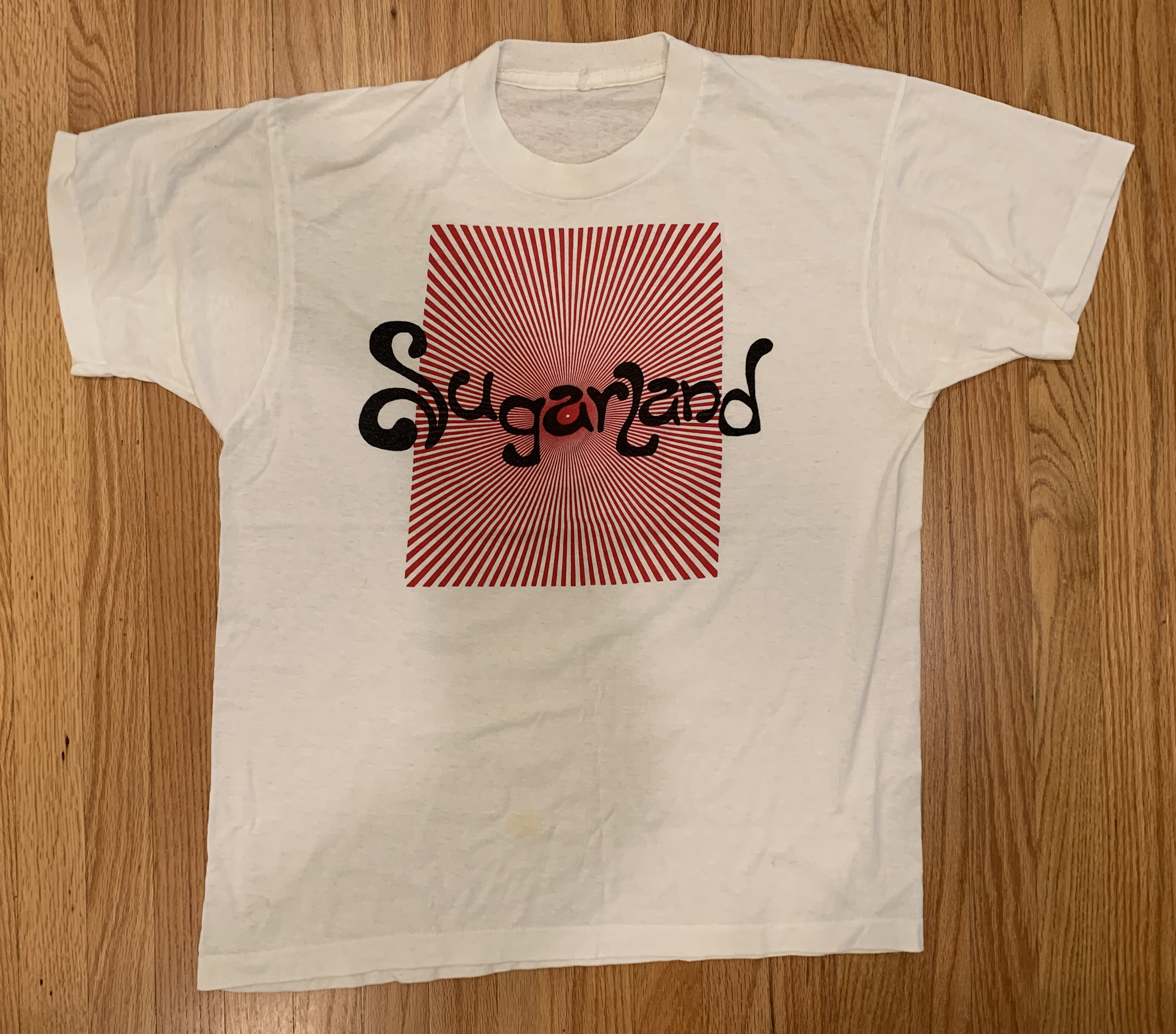 A white shirt with the same logo, in black, in front of a red radial striped background