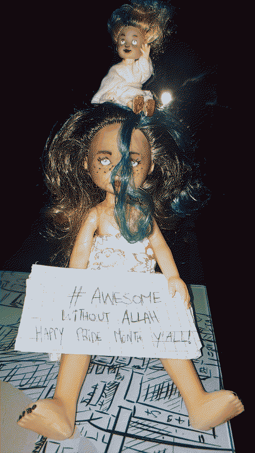 My two custom dolls, Rosalinda-s, sitting holding a sign that reads # Awesome Without Allah Happy Pride Month Y'All