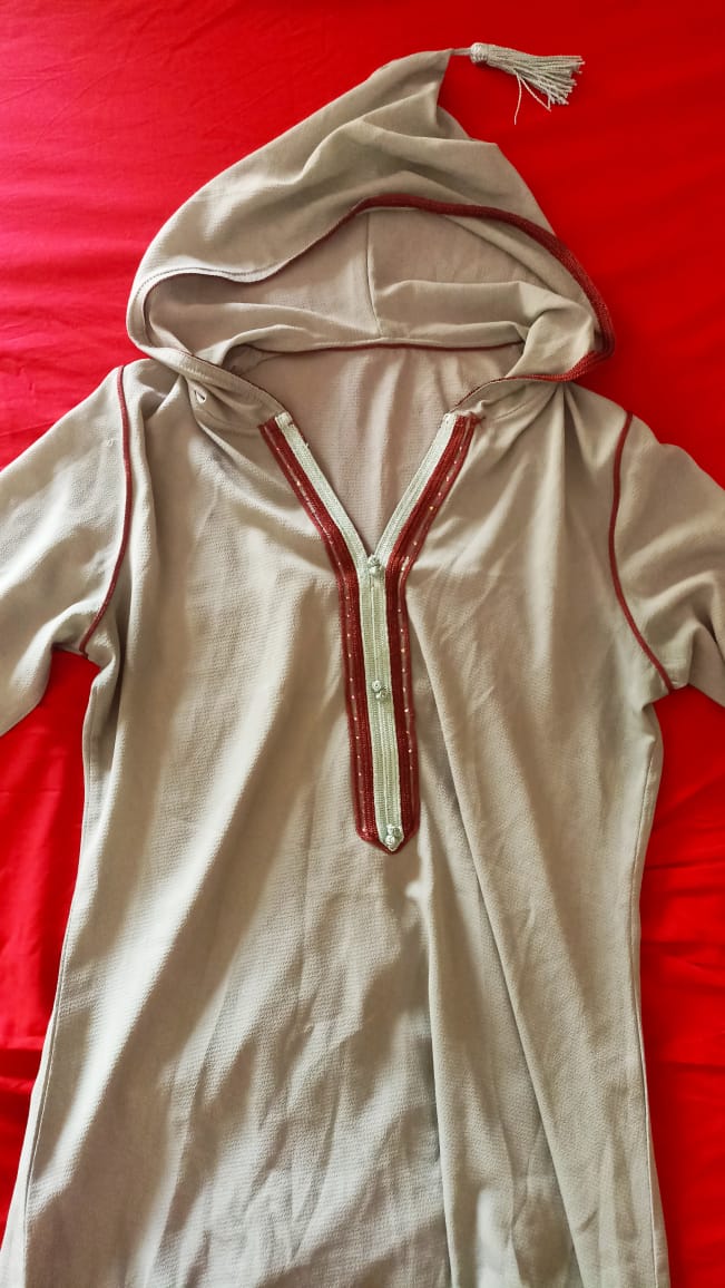 A traditional Moroccan jelaba laid out flat on a red surface