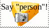 a white stamp with an image of a cheese holding a camera saying 'say person!'