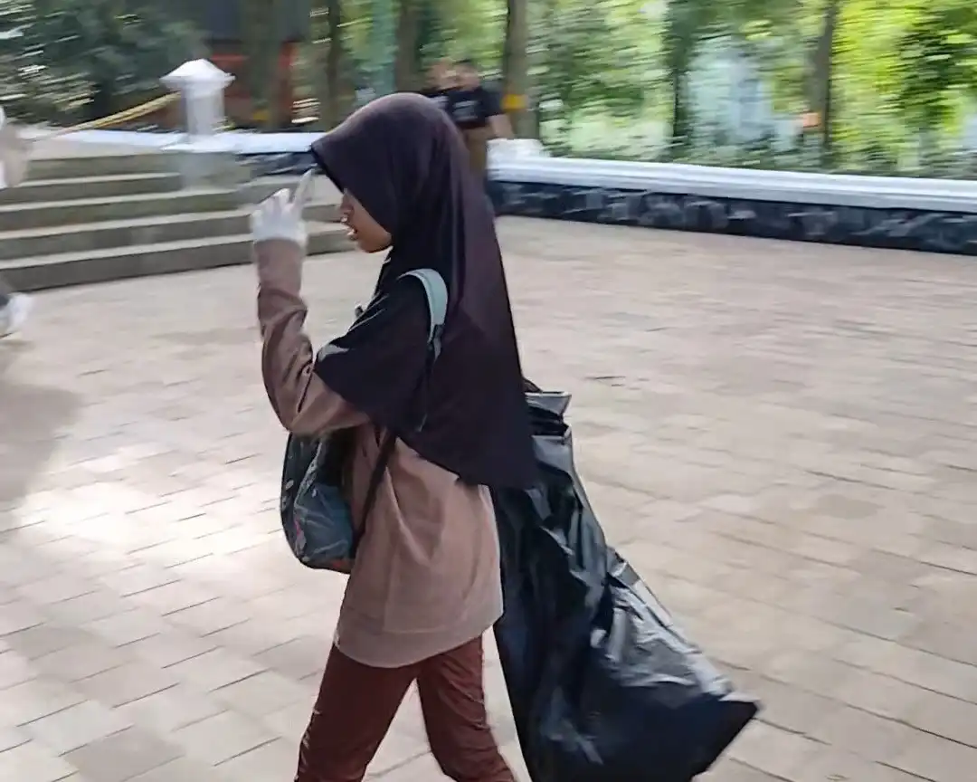 Seorang perempuan remaja mengenakan hijab berjalan di Tahura sambil membawa kantong sampah berwarna hitam