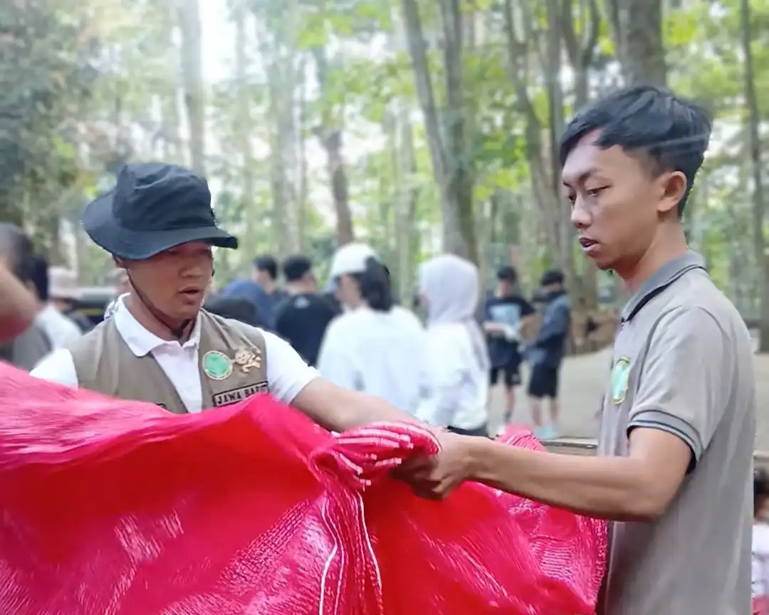 Dua pria membentangkan kantong jaring merah di area tahura saat kegiatan luar ruangan.