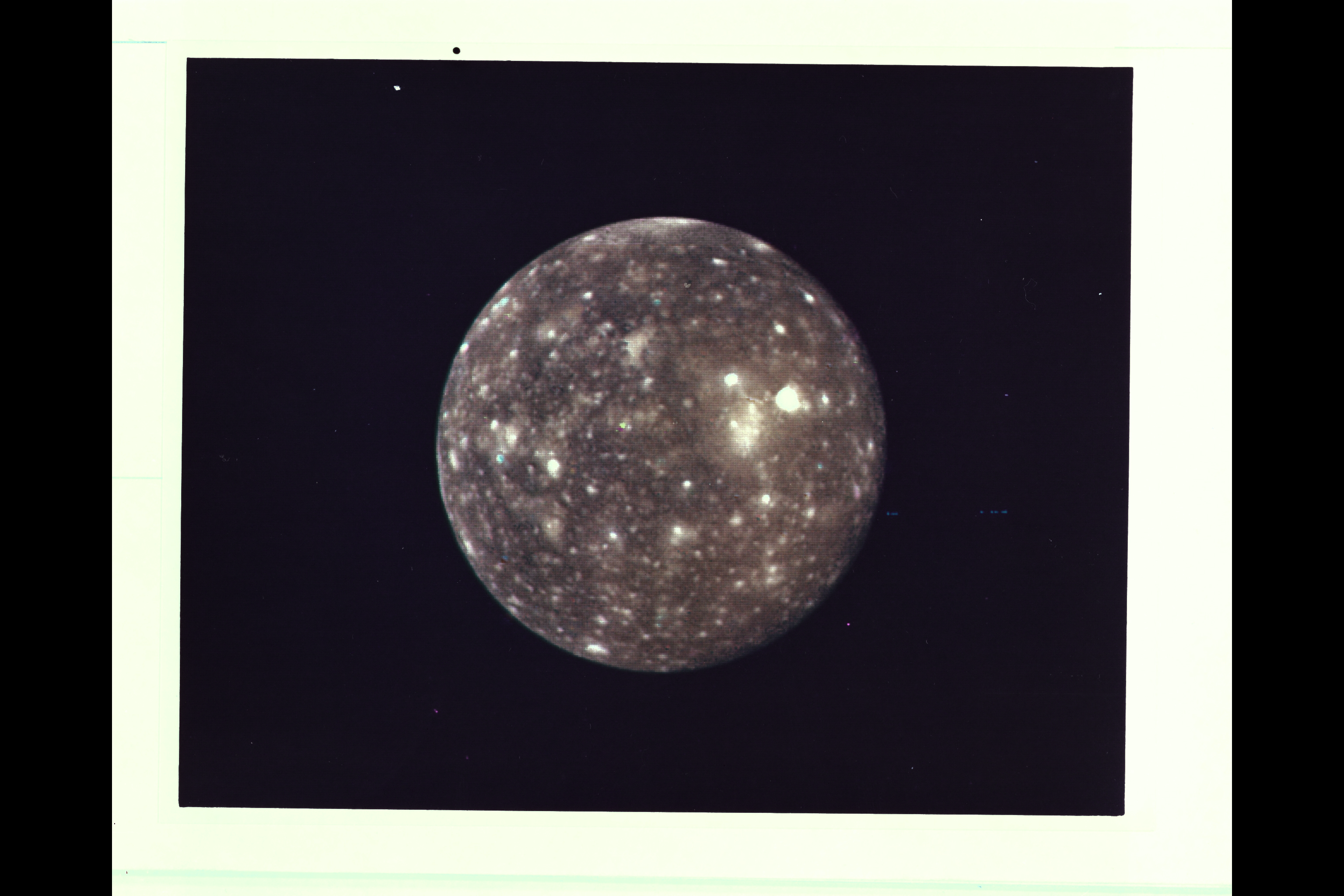 A photo of a moon on film.
Range: 2,318,000 kilometers (1,438,000 miles)
This picture of Callisto taken by Voyager 2 shows the moon covered with bright spots which are metoerite impact craters--a fact originally discovered from the high resolution pictures taken by Voyager 1. Scientists believe that heavily cratered terrains like these on Callisto are indicative of ancient planetary surfaces. Voyager 2 mapped the side of Callisto not seen by Voyager 1. The obsure dark streaks in this area may be fault zones, but higher resolution pictures are needed for identification.