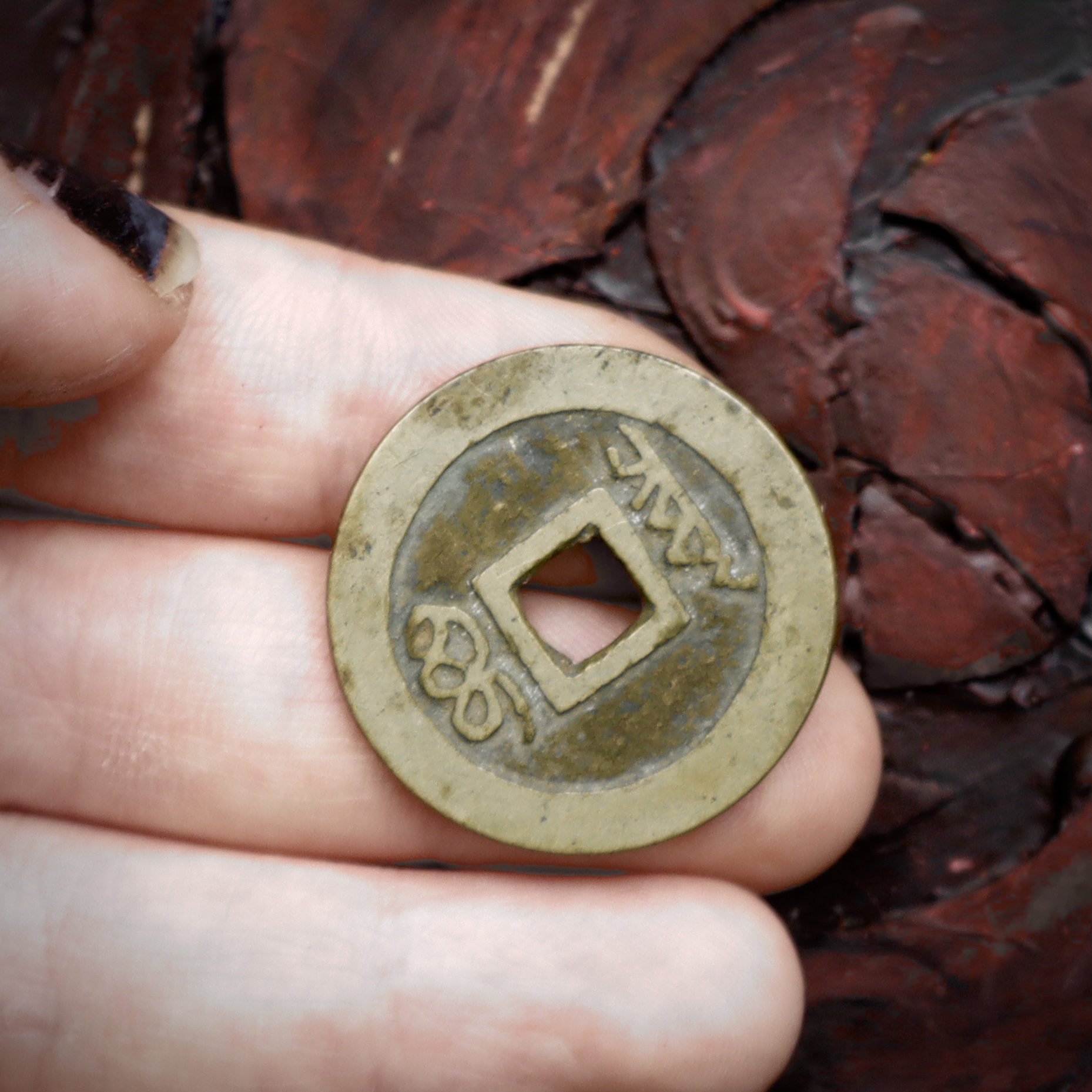 An old brass coin, with a square hole in the middle. In the middle, there are raised characters on either side of the hole.
