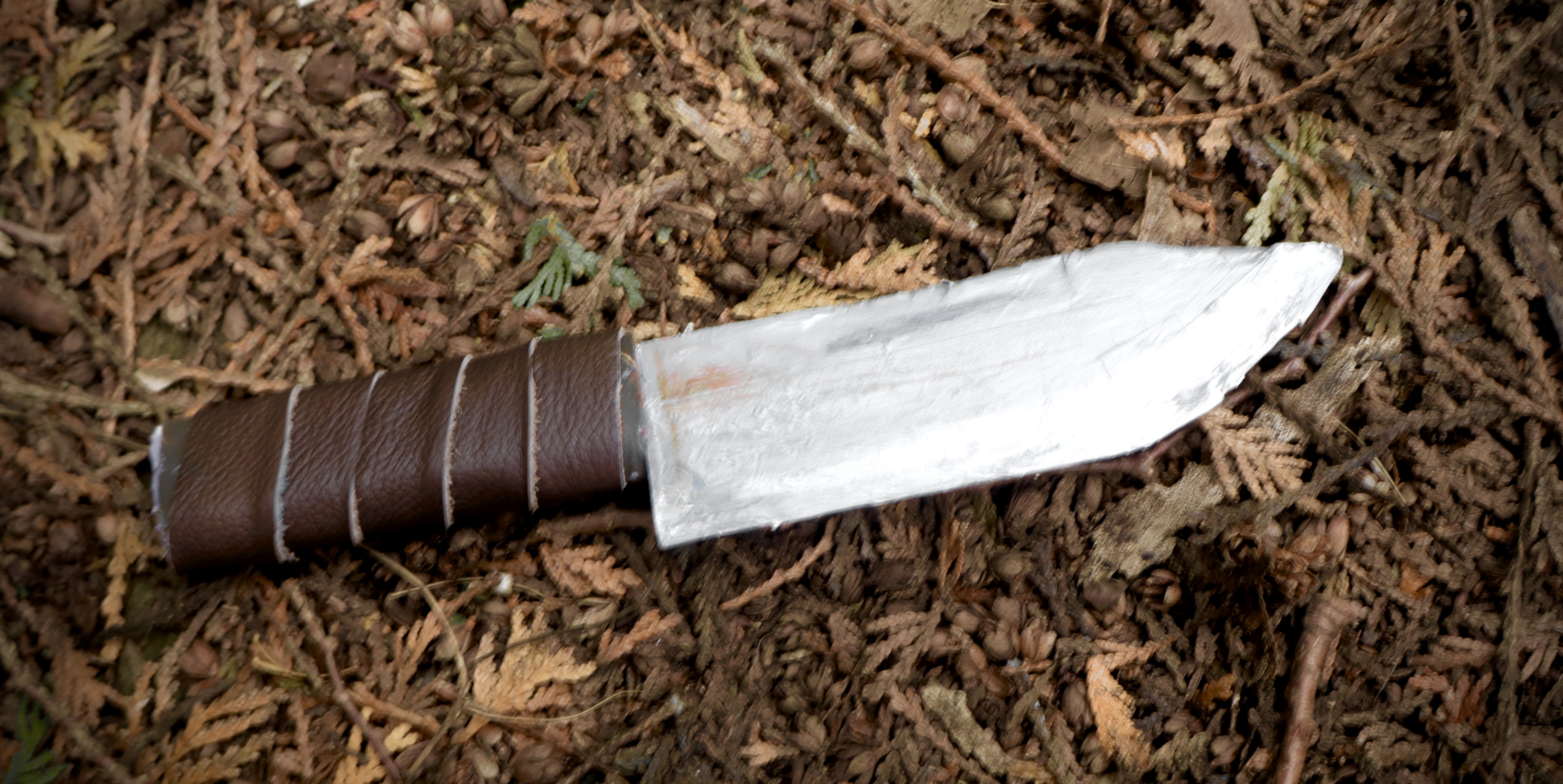 A small one-sided blade, painted grey with some rusting near the base. The handle is wrapped in brown leather.