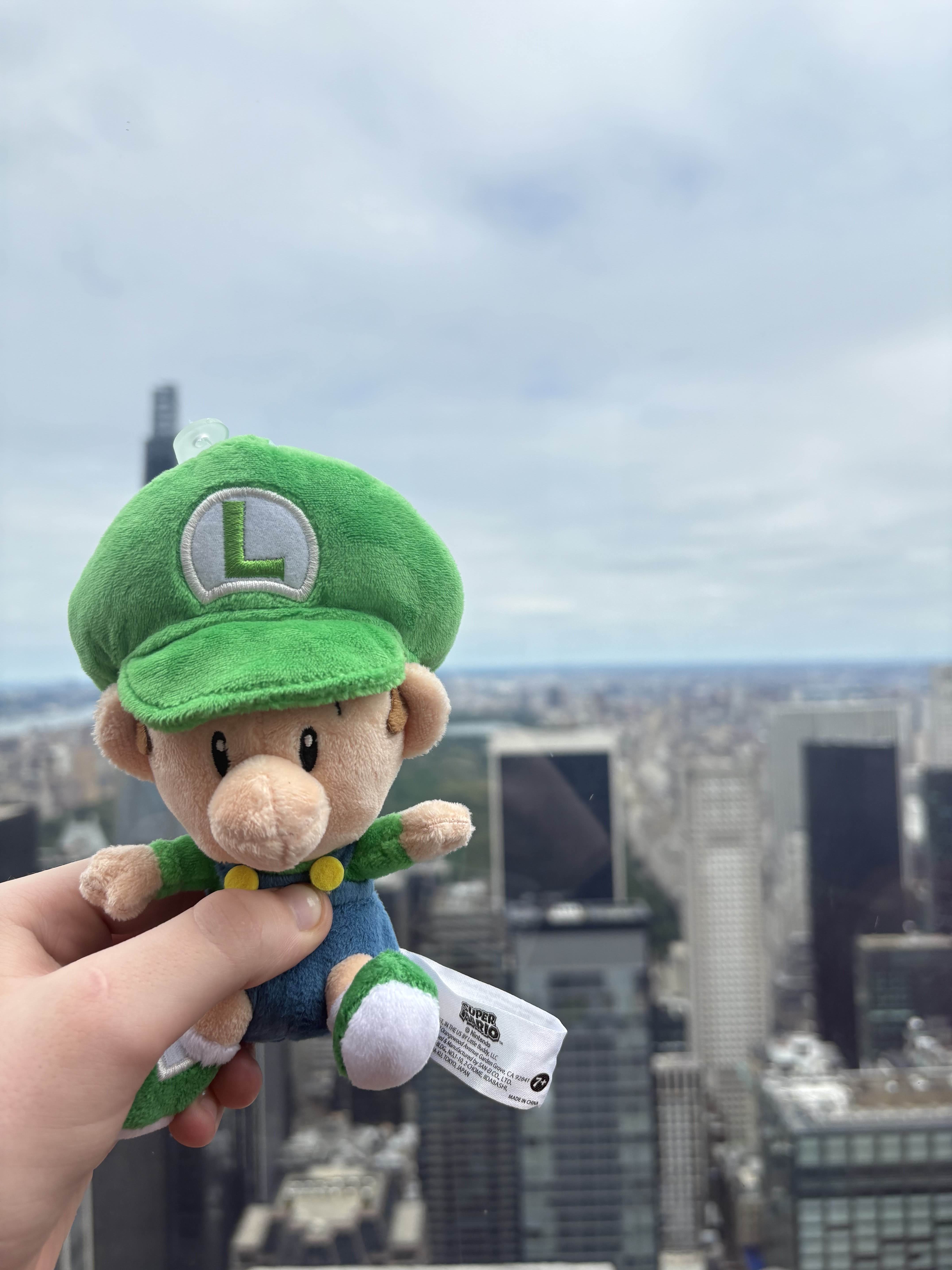 a plush of baby luigi with a nyc backdrop