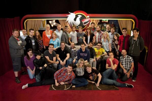 A picture of a large group of people in a room with red flooring and red wallpaper. They're all generally looking in the camera's direction.