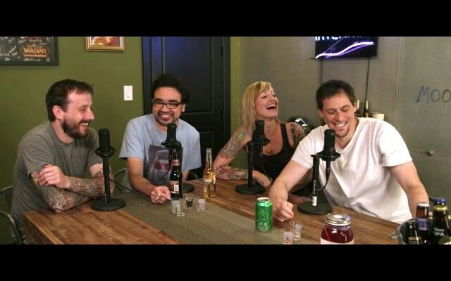 A picture of four people sat around a table in a room with green wallpaper. The four people have mics around them. All four are smiling and laughing.