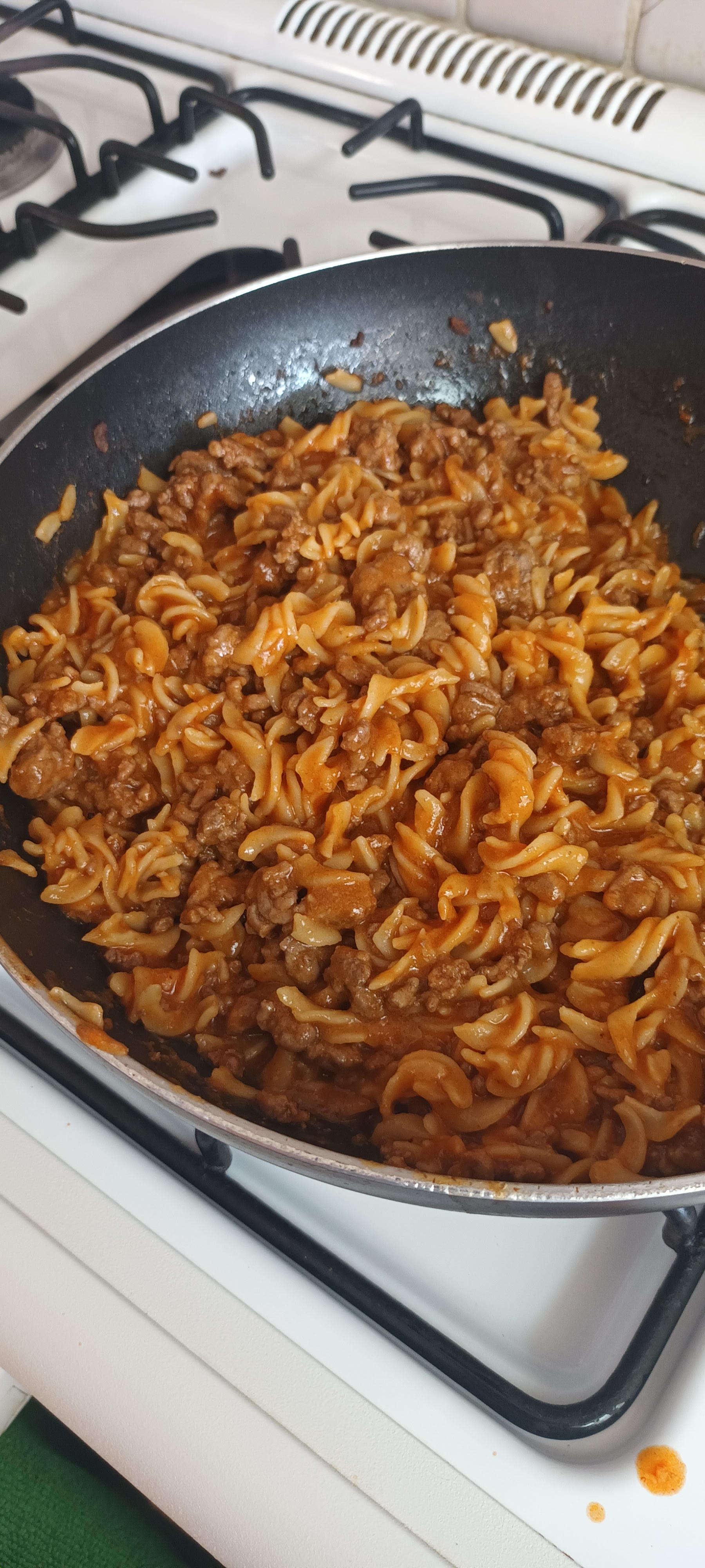A plate of fusilli pasta in a black pan resting on a stove cooked with tomato sauce and pieces of minced meat