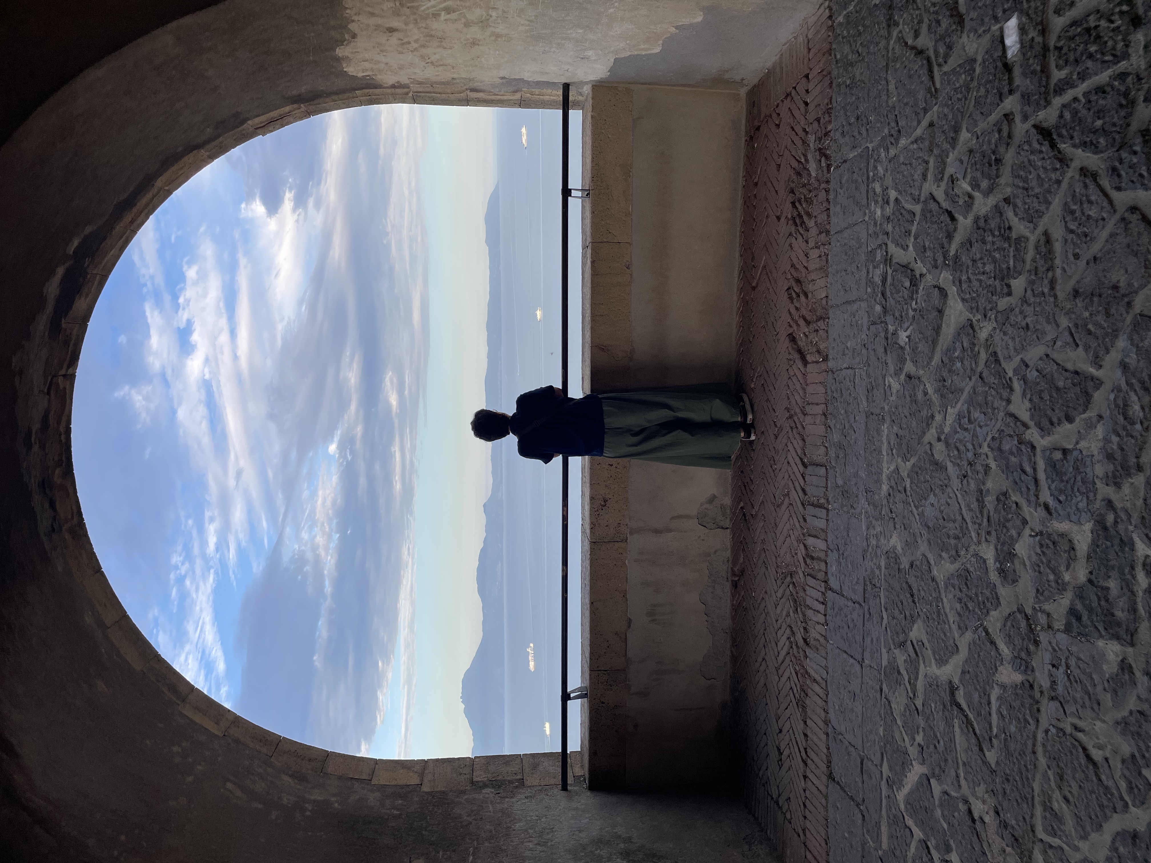 A person from behind looking at the gulf of Naples from an arch window.