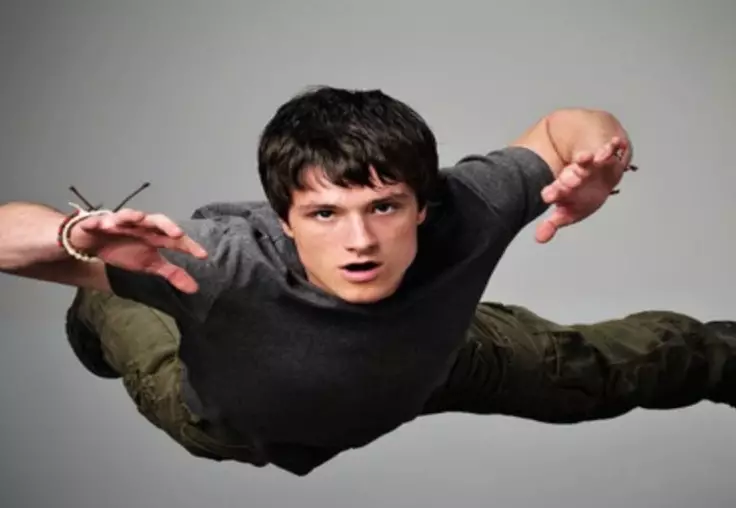 Josh Hutcherson is in a grey shirt and black pants. He lies flat on his stomach, though, he does not touch the ground. He is depicted as floating. However, the look on his face is of worry or fear, he stare into the camera. He is falling.